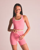Woman wearing a pink athletic outfit holding a straw against a plain background